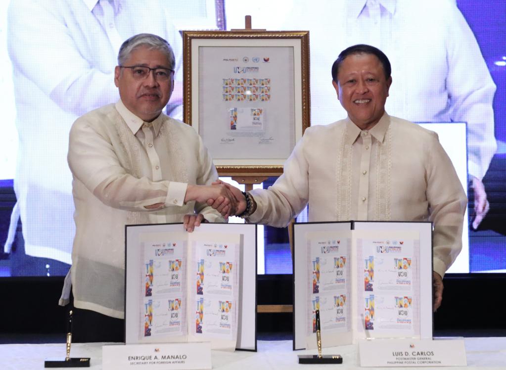 Two men shake hands while displaying stamps