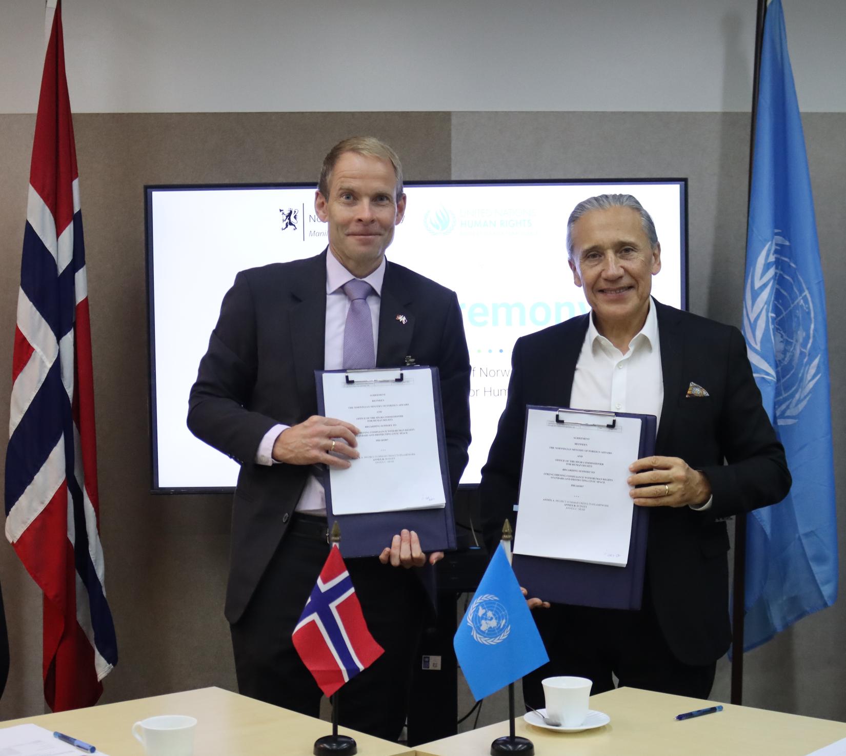 The Norwegian Ambassador and UN Philippines Resident Coordinator stand side-by-side holding copies of an agreement they have just signed.