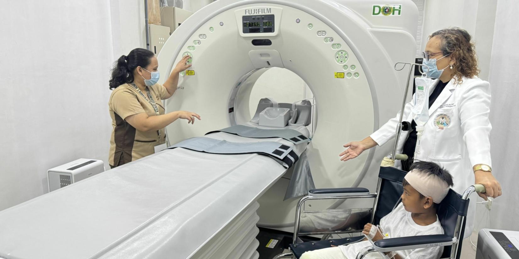 A child patient in a wheel chair is assisted by female medical personnel to undergo CT Scan procedure 