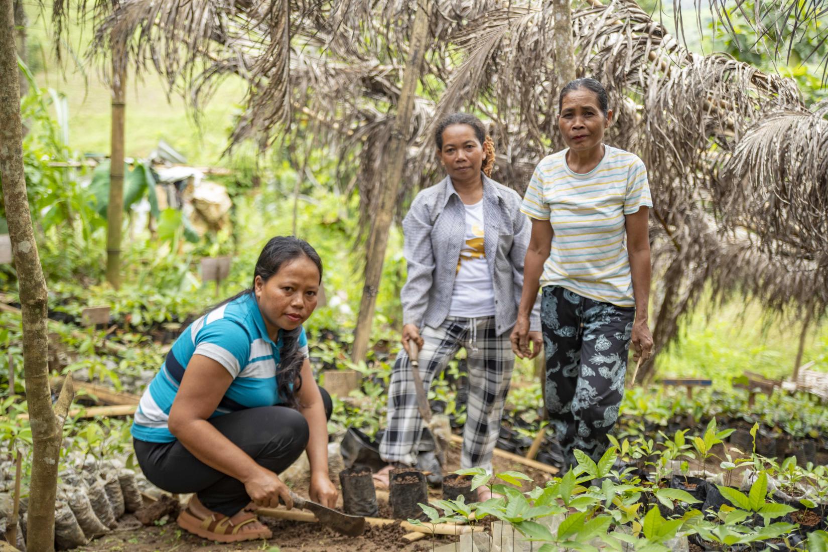 Three women practice climate resilient farming / planting.