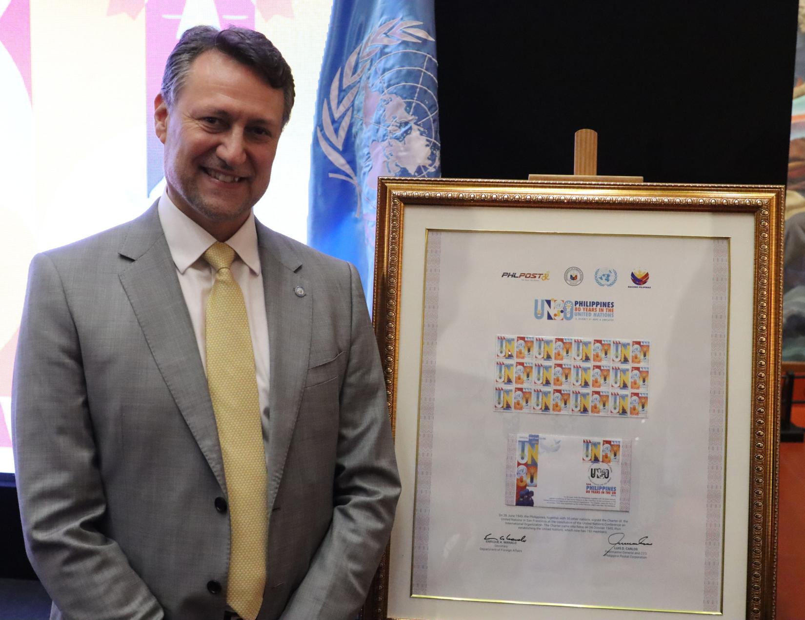 Man poses next to framed commemorative stamps 