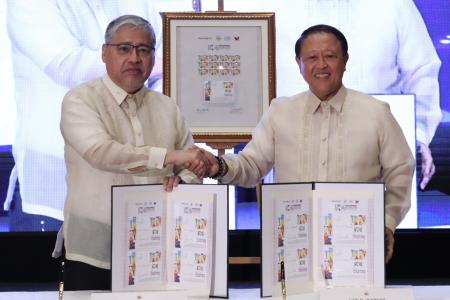 Two men shake hands while displaying stamps