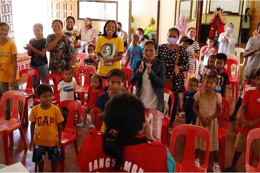 Community volunteer Norina (mid-frame, in yellow) participates in a ceremonial distribution of birth certificates for Sama Bajau children in Brgy. Tubig Tanah, Patikul, Sulu